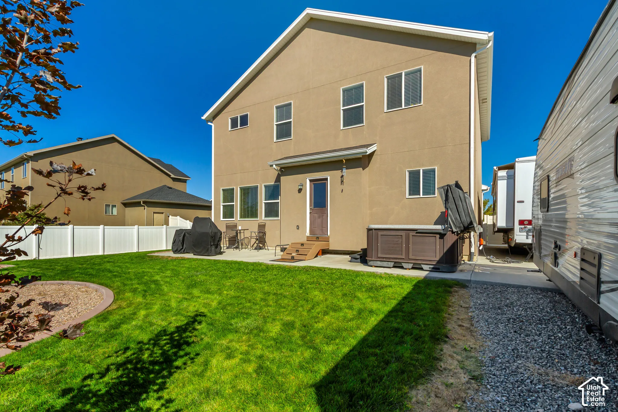 Expansive backyard featuring a manicured lawn, white privacy fencing, and a concrete patio