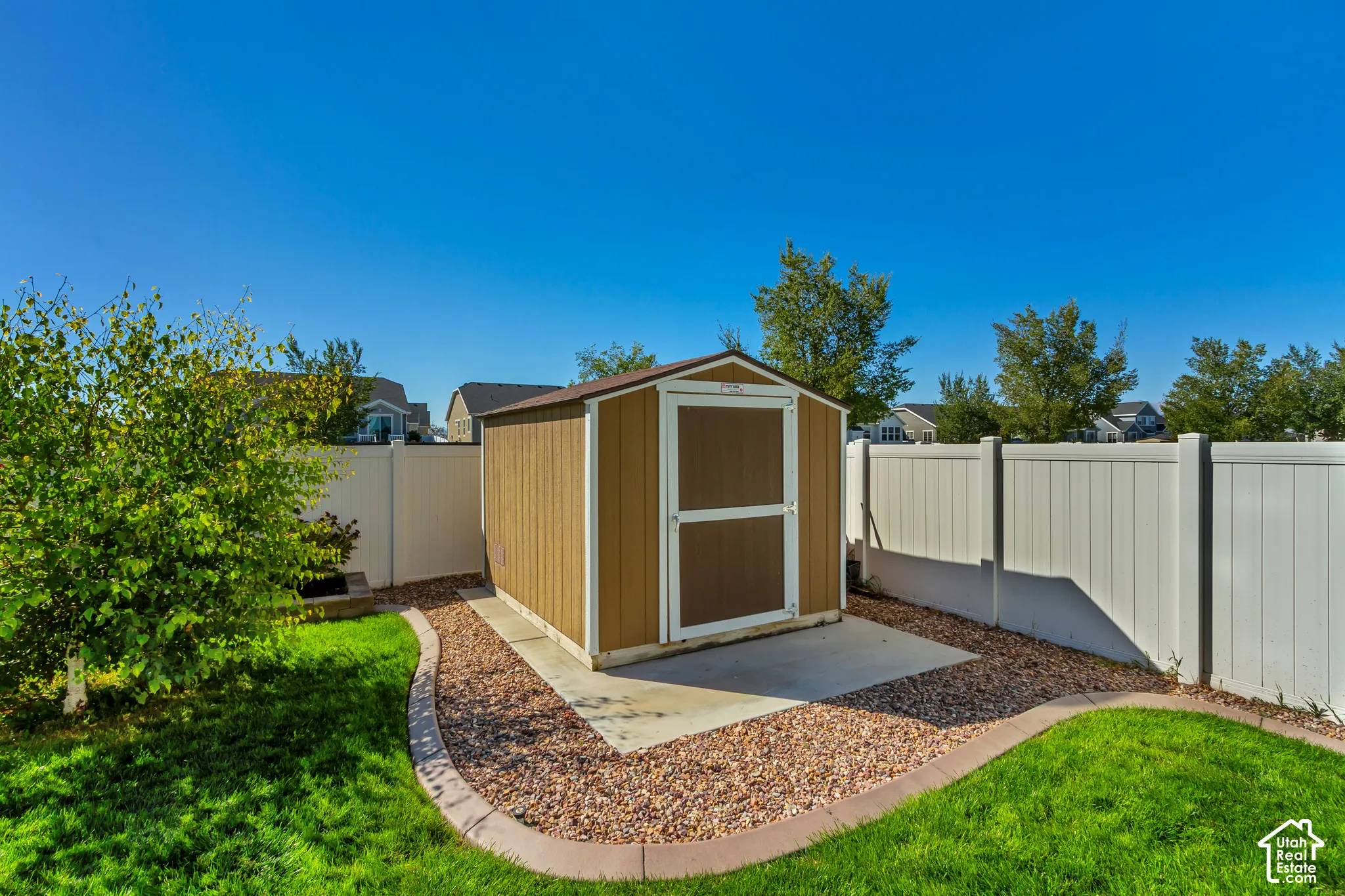 Backyard featuring a shed with a concrete pad, gravel landscaping, a manicured lawn, and a white privacy fence