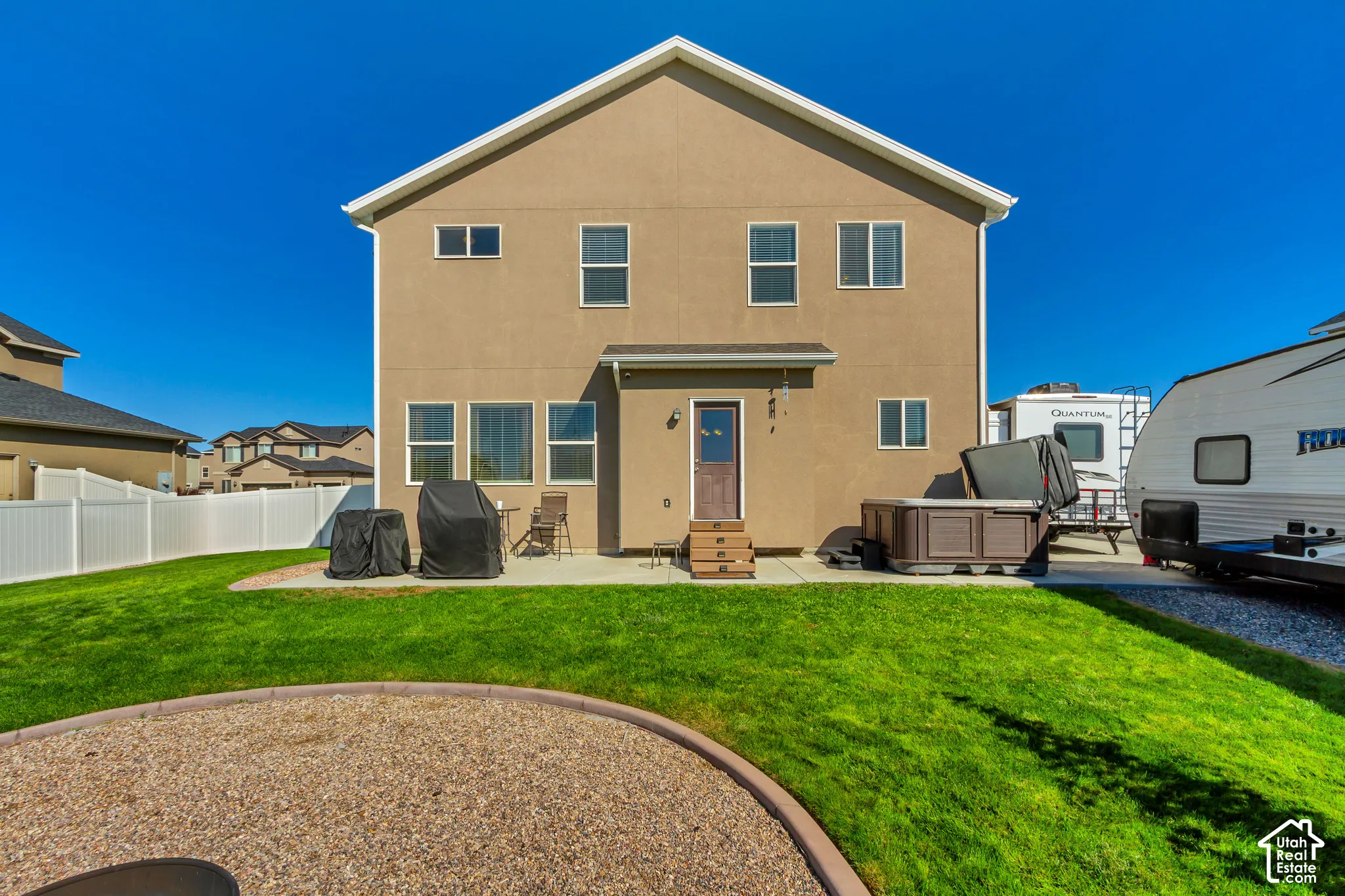 Expansive backyard with a manicured lawn, concrete patio, and a white vinyl fence