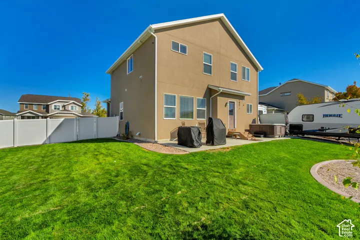 Expansive grassy backyard featuring a white privacy fence, concrete patio, and a built-in hot tub