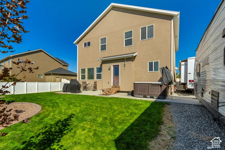 Expansive backyard featuring a manicured lawn, white privacy fencing, and a concrete patio