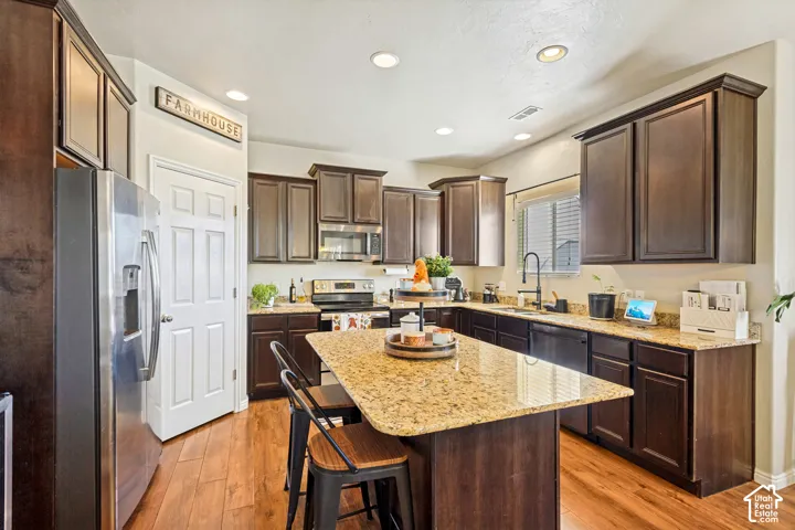 Kitchen featuring wood-finish flooring, dark wood cabinetry, a granite-style island, and recessed lighting
