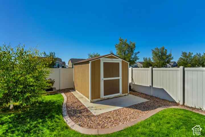 Backyard featuring a shed with a concrete pad, gravel landscaping, a manicured lawn, and a white privacy fence