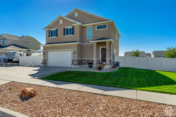 Two-story stucco exterior with stone accents, attached two-car garage, covered entry, and manicured lawn