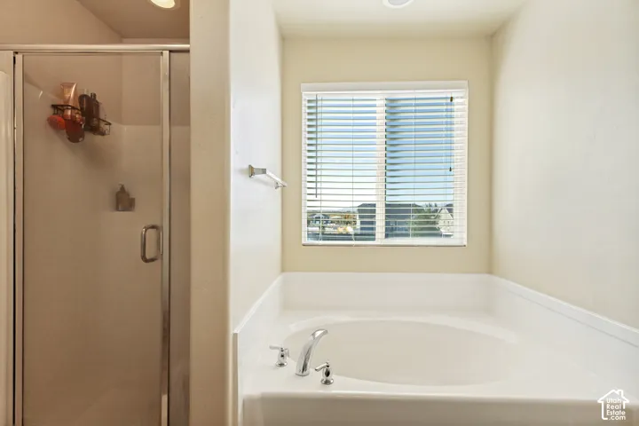 White built-in soaking tub with chrome fixtures, an adjacent glass-enclosed shower, and a window with horizontal blinds