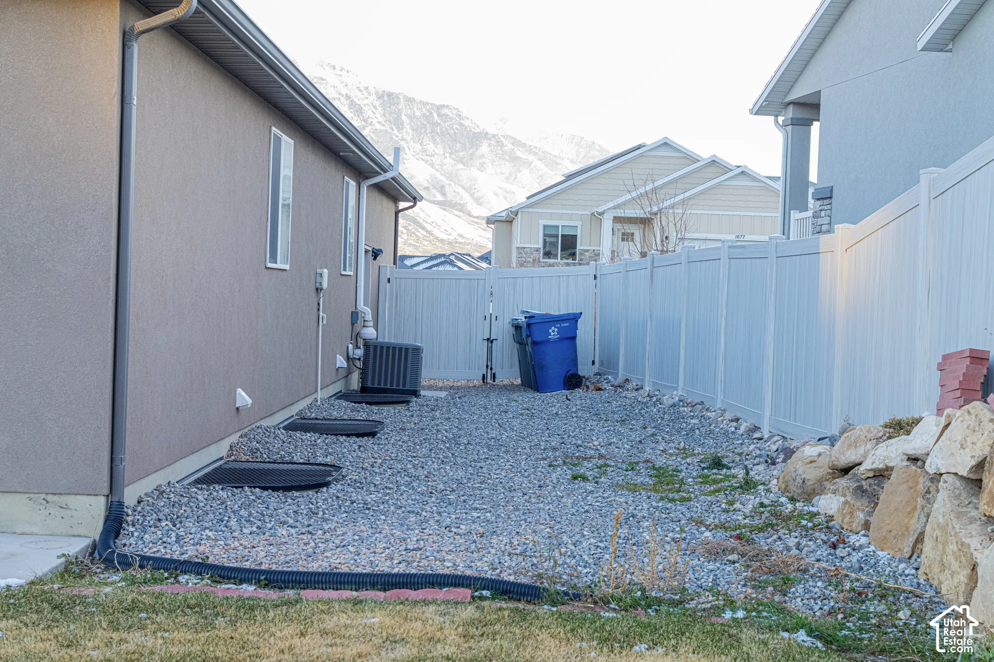 Stucco exterior with white-framed windows, gravel landscaping, and a white vinyl privacy fence