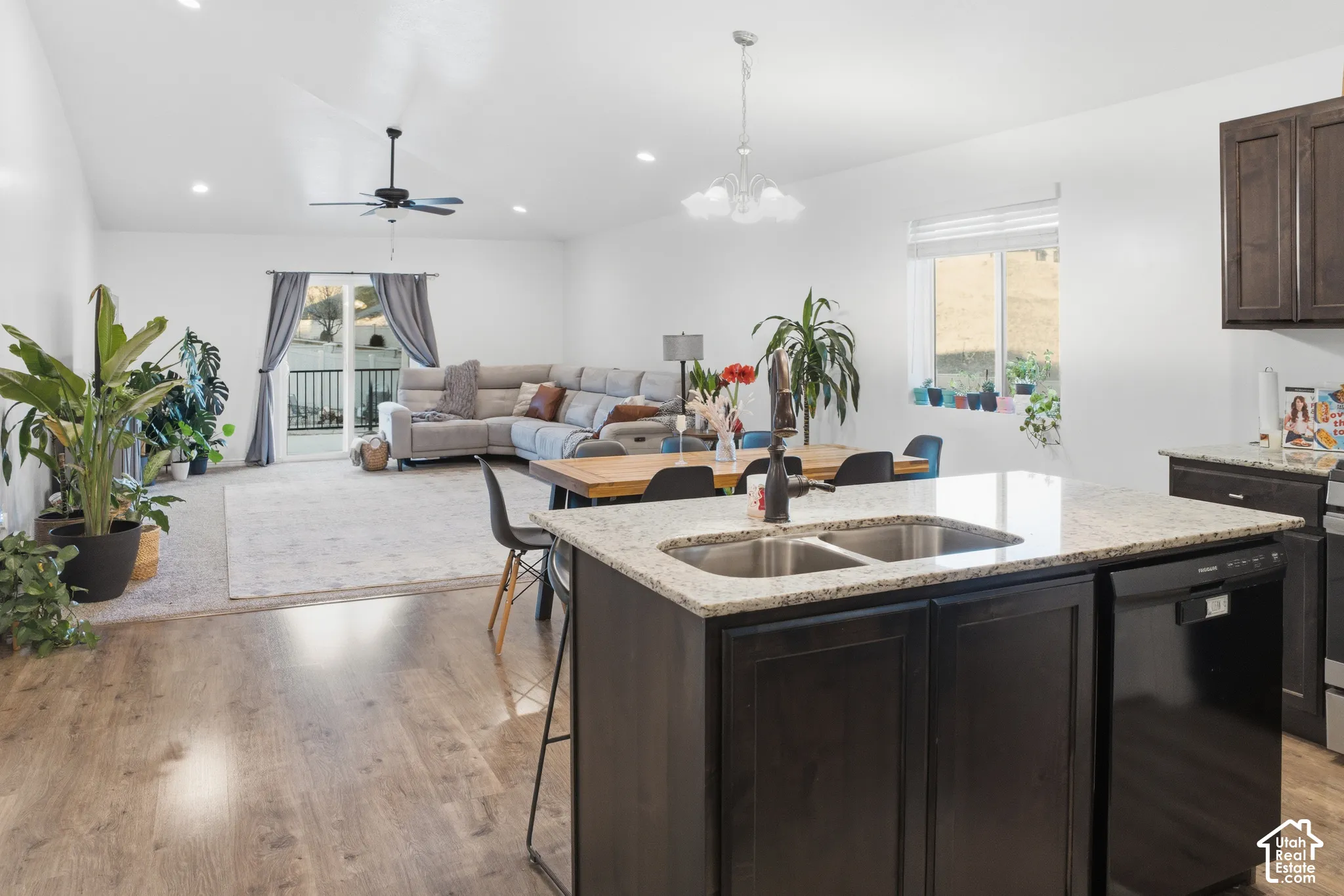 Wood-finish flooring, kitchen island with dual basin sink, integrated dishwasher, dark cabinetry, and recessed lighting