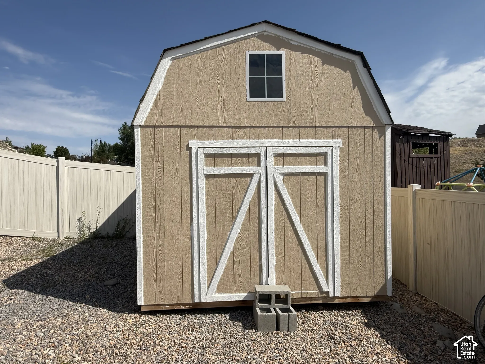Gambrel-style shed with double doors and an upper window, set on a gravel base