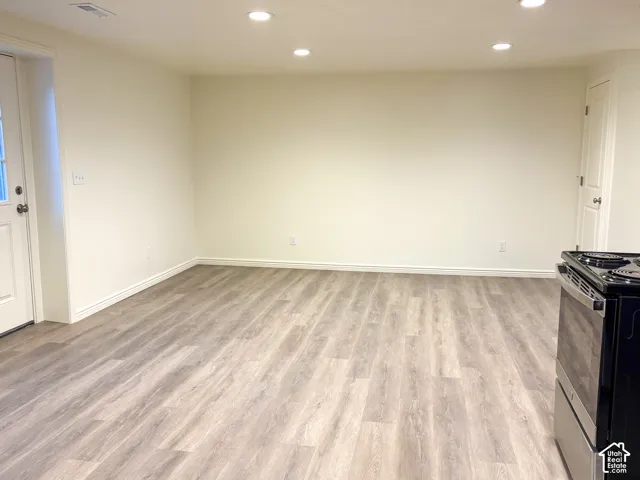 Recessed lighting illuminates the expansive room featuring wood-finish flooring and a white paneled door