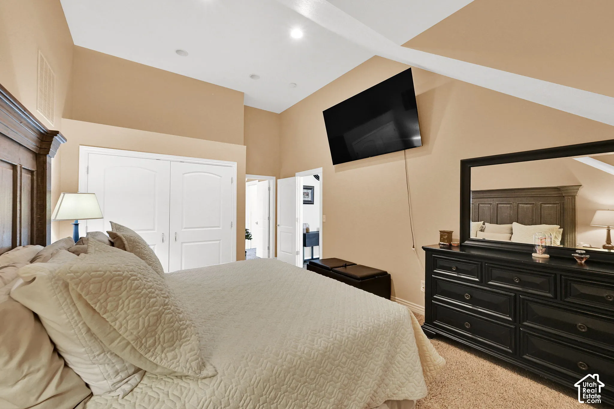 Vaulted ceiling with recessed lighting, neutral wall tones, white bi-fold closet doors, and carpeted flooring