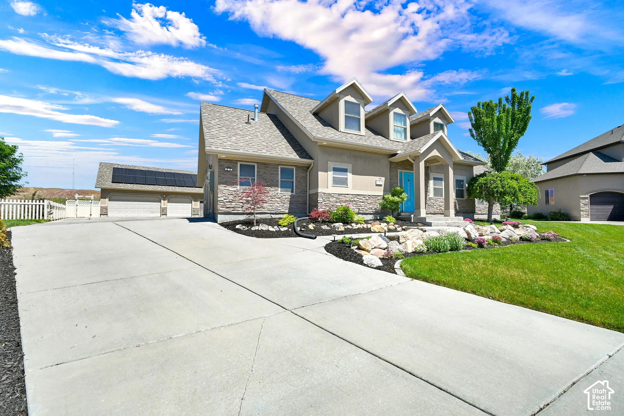 Multi-level residence with a large concrete driveway, stone facade accents, dormer windows, and a vibrant turquoise front door