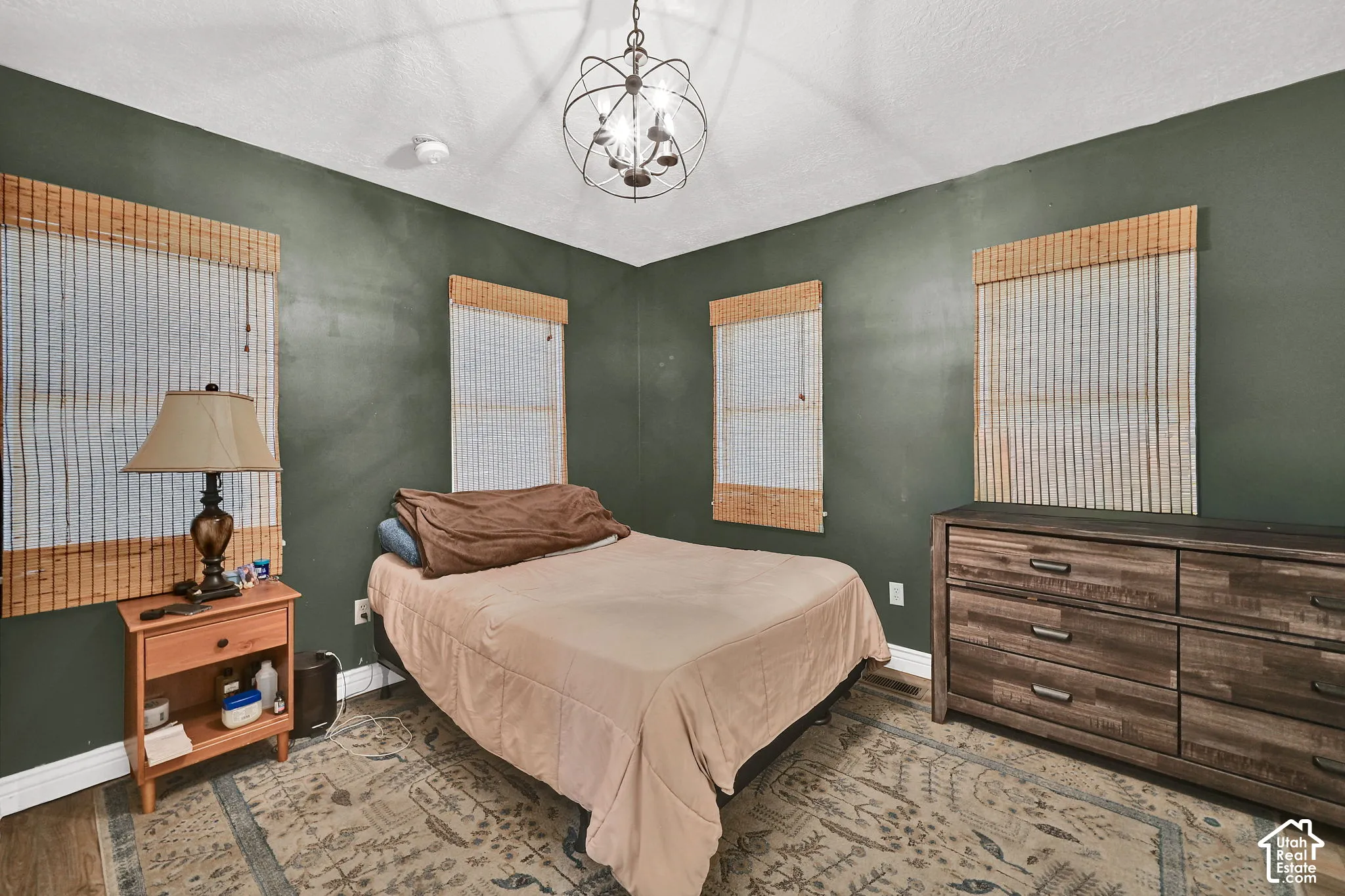 Dark green wall finish, wood-finish flooring, two window openings, and an orb chandelier