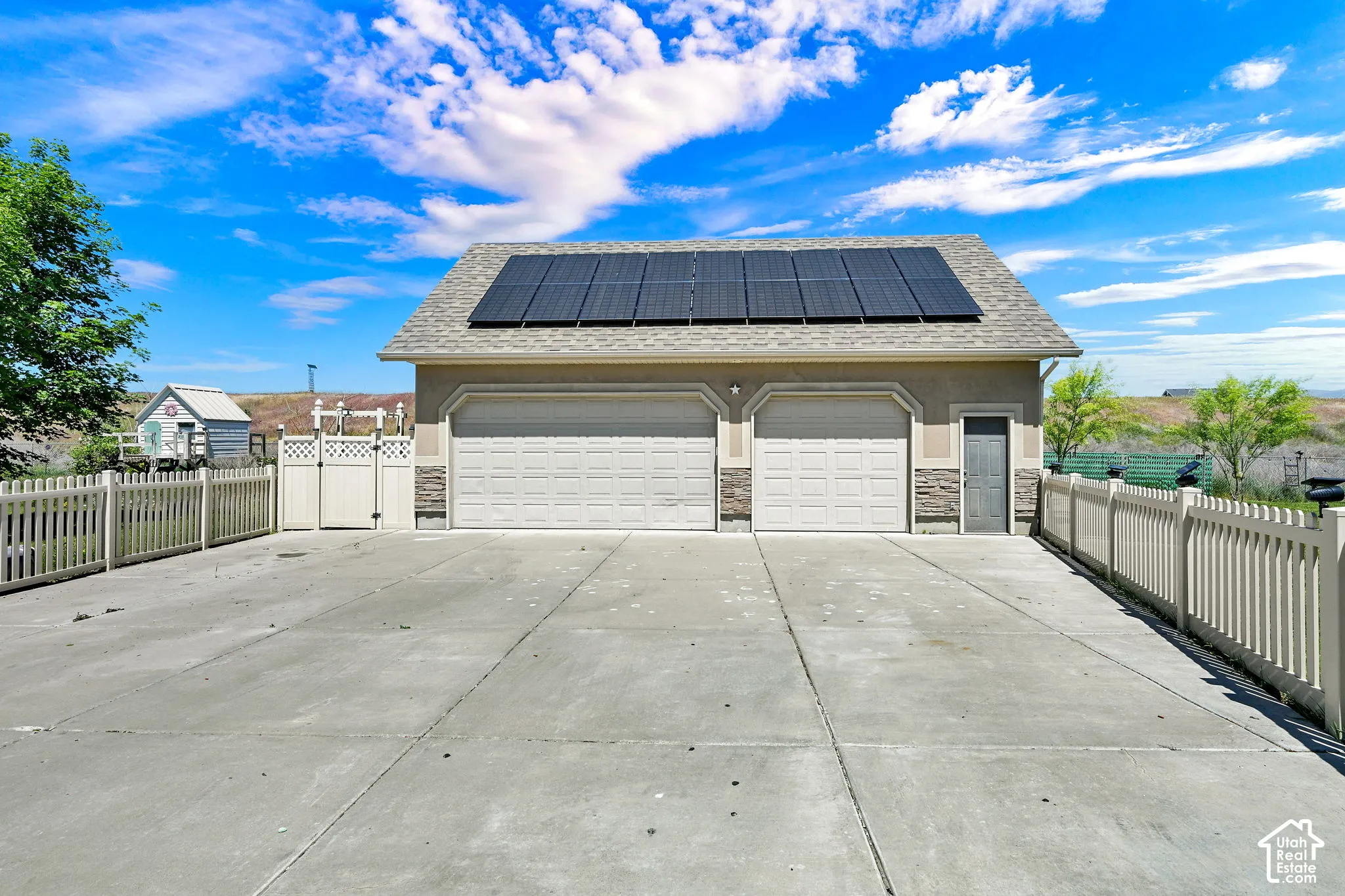 Detached garage featuring dual bay doors, rooftop solar panels, stucco exterior with stone accents, and an adjacent utility door