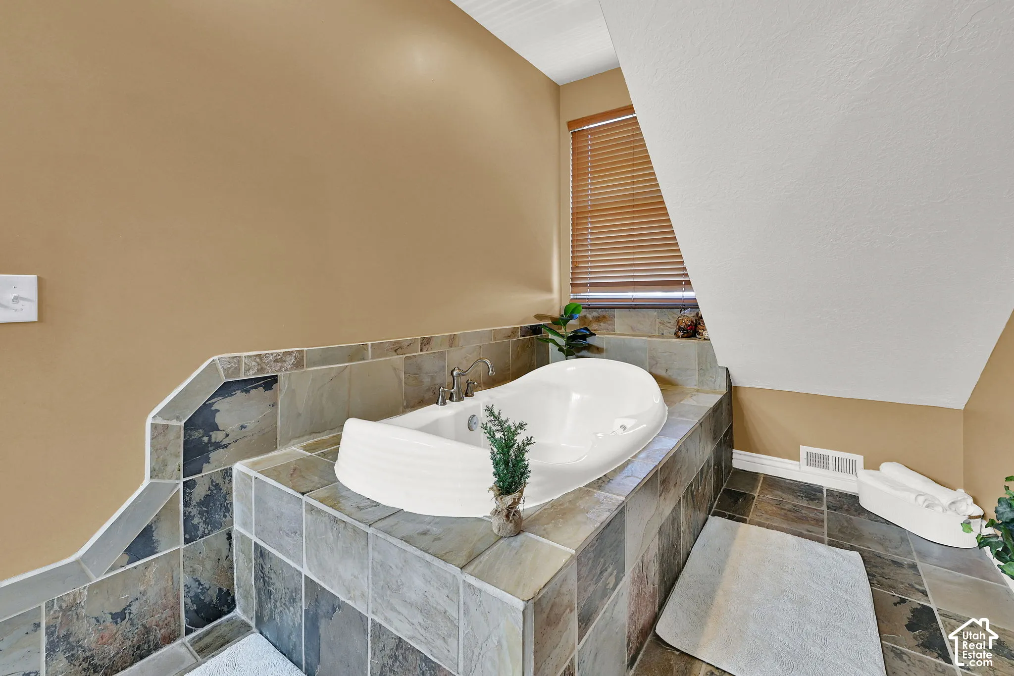 Built-in soaking tub with deck-mounted fixtures, surrounded by natural stone tile
