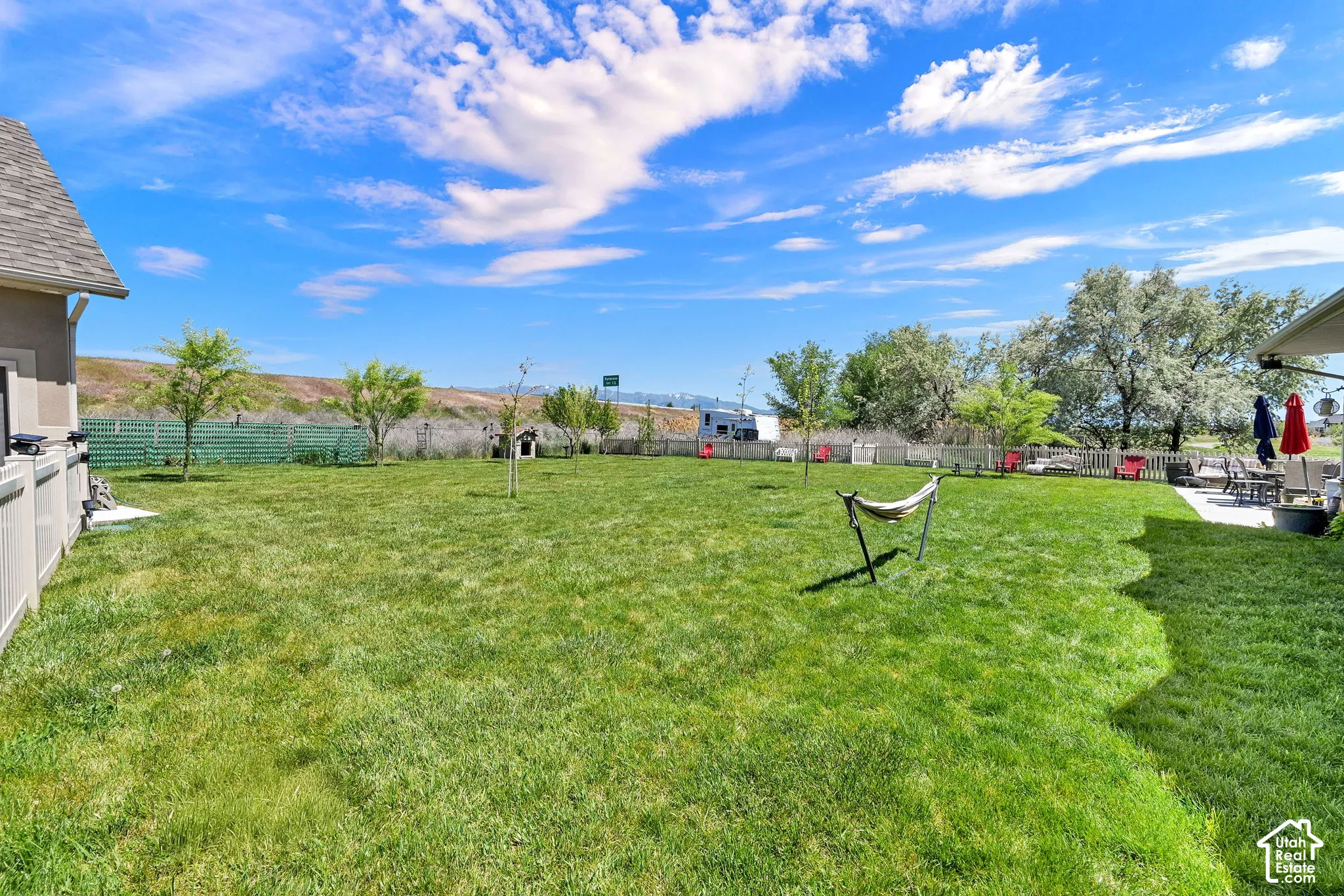 Expansive green lawn with a privacy fence, established trees, and a concrete patio