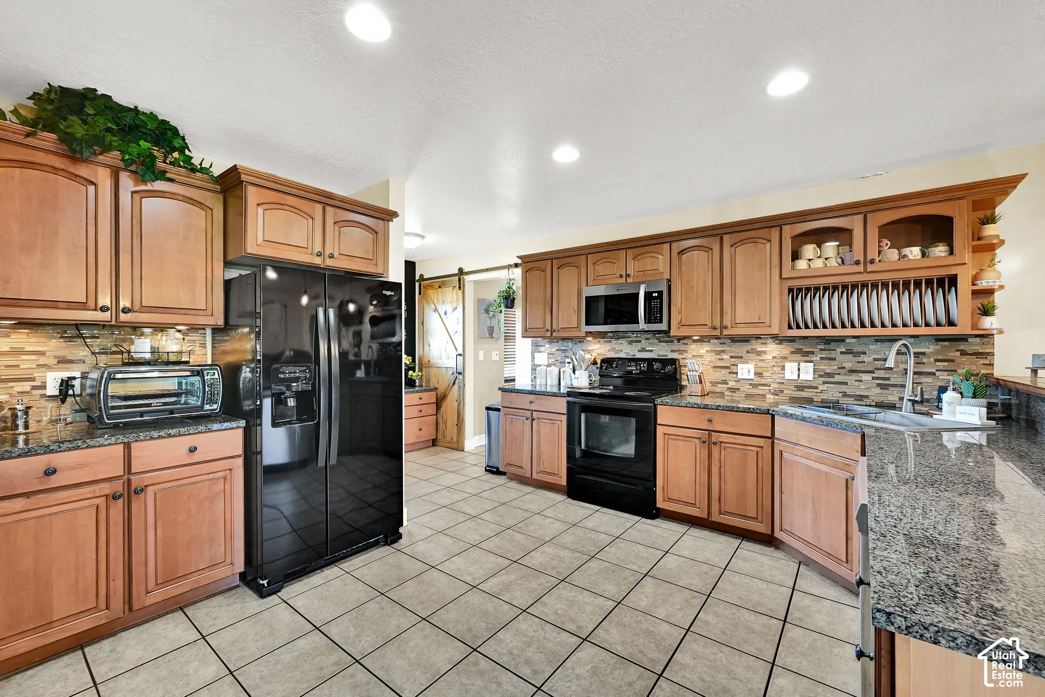 Gourmet kitchen featuring wood cabinetry, stone countertops, a tile backsplash, tile flooring, and integrated black appliances