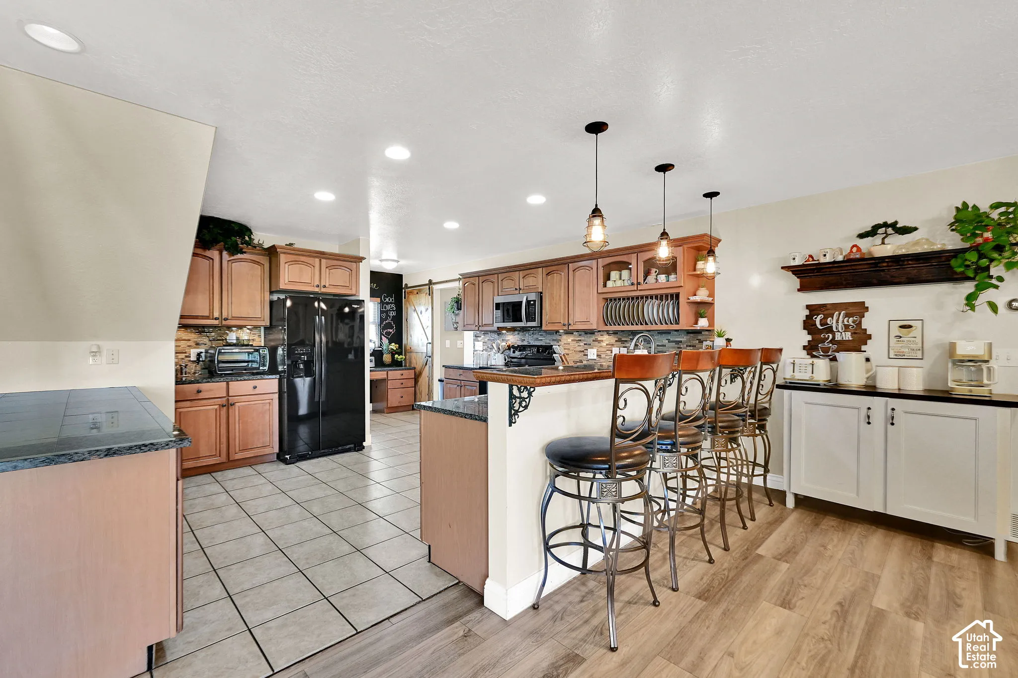 Kitchen featuring tile flooring, wood-finish cabinetry, granite-style countertops, recessed lighting, and a breakfast bar