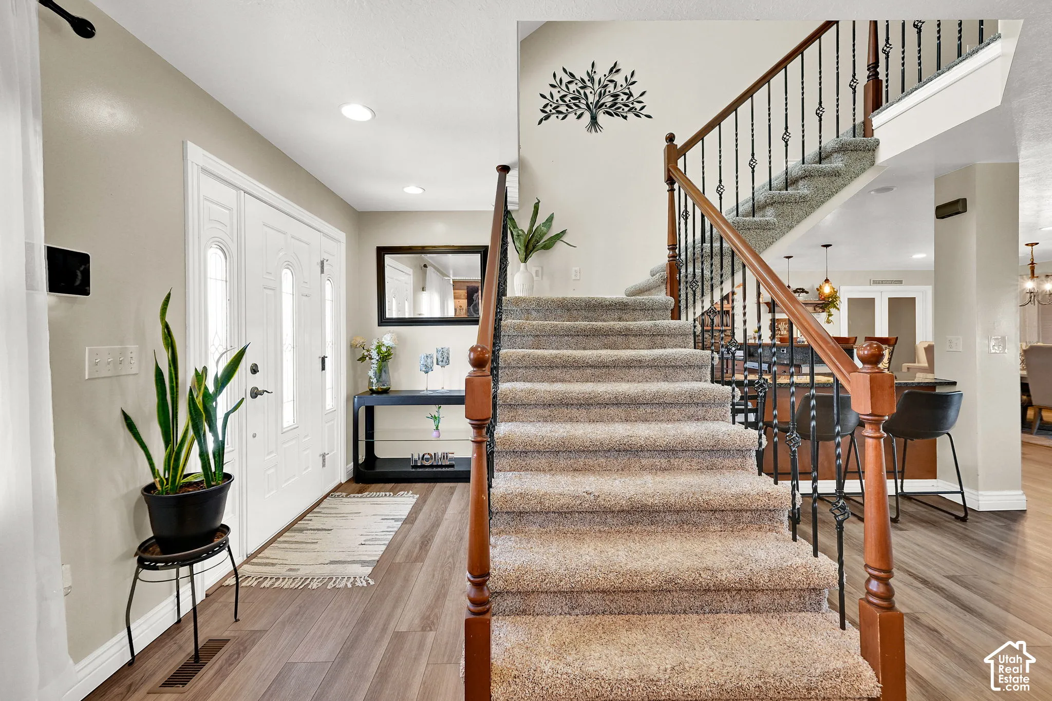 Entryway featuring a double door with decorative glass inserts, wood-finish flooring, recessed lighting, and a carpeted staircase with wrought iron balusters and a wood handrail