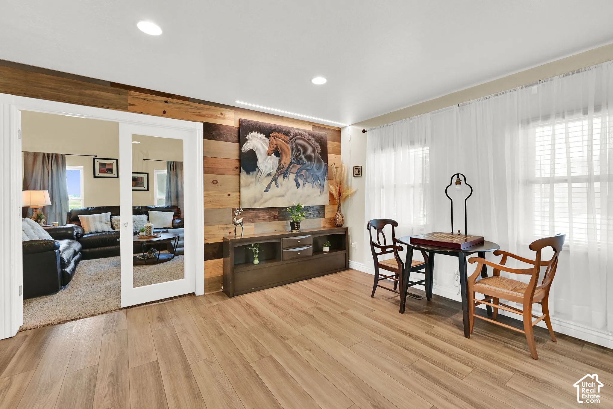 Recessed ceiling lighting, wood-finish flooring, accent wall with wood paneling, sliding glass panel door, and multiple windows with blinds