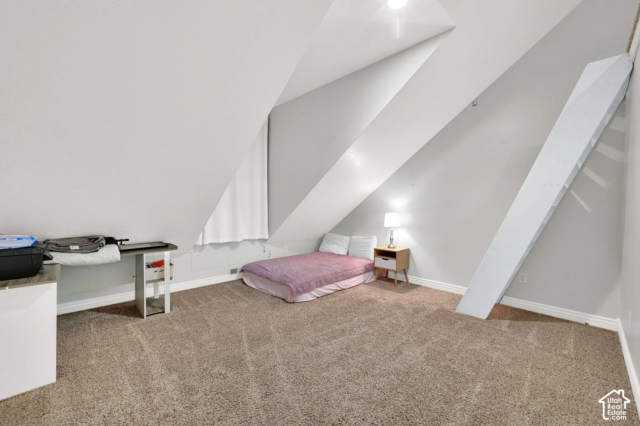 Carpeted attic space featuring sloped ceilings, a window with a white curtain, and light-colored wall paint