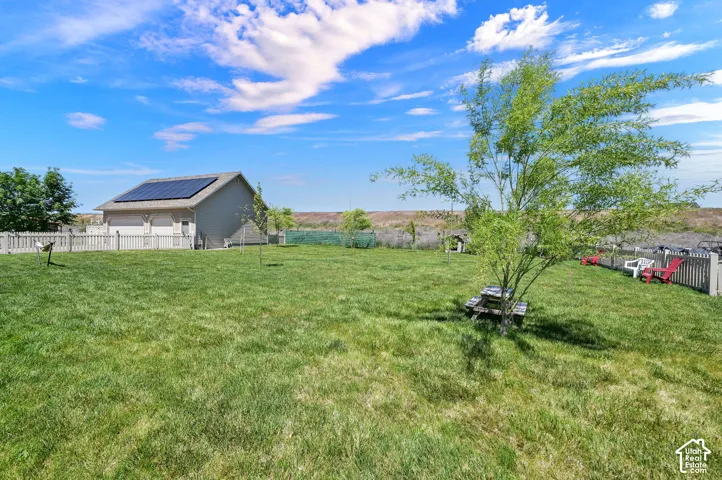 Expansive grassy yard with a white picket fence, mature tree, and solar panels on the roof