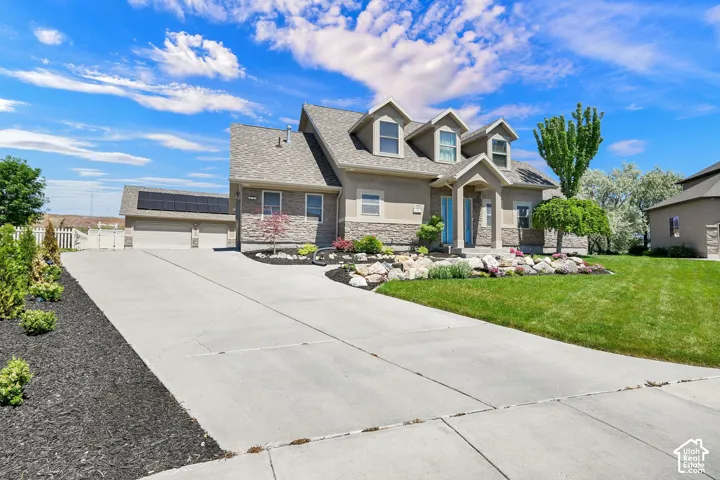 Stucco and stone exterior with dormer windows, a concrete driveway, and established landscaping