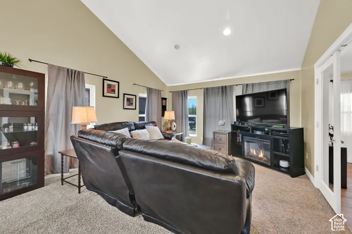 Vaulted ceiling, recessed lighting, carpet flooring, and a built-in media console with an electric fireplace