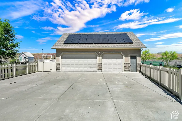 Detached garage featuring dual bay doors, rooftop solar panels, stucco exterior with stone accents, and an adjacent utility door