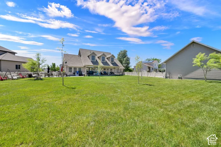 Expansive green lawn with young trees, white privacy fencing, and a covered back patio