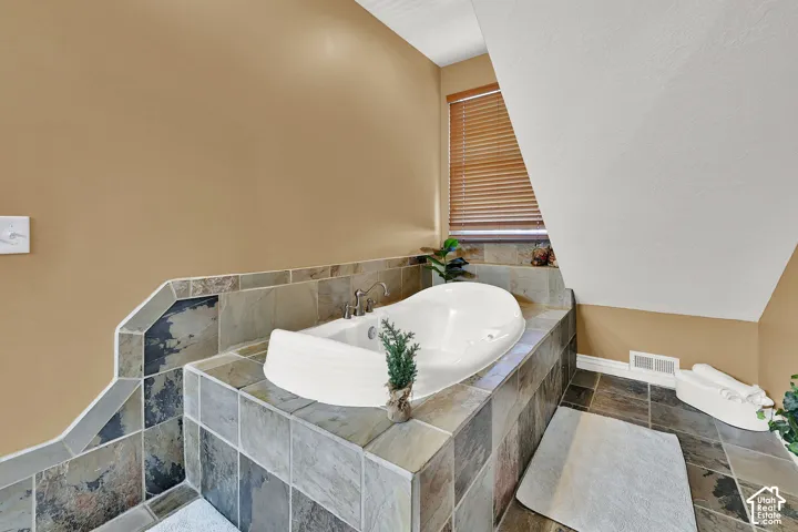 Built-in soaking tub with deck-mounted fixtures, surrounded by natural stone tile
