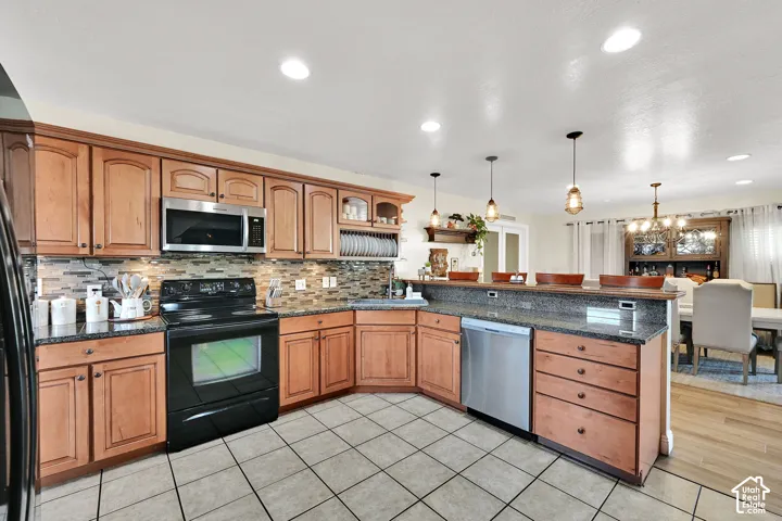 Kitchen featuring wood-finish cabinetry, stainless steel appliances, tiled backsplash, granite countertops, and recessed lighting