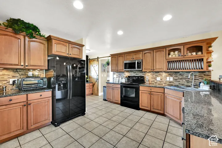 Gourmet kitchen featuring wood cabinetry, stone countertops, a tile backsplash, tile flooring, and integrated black appliances