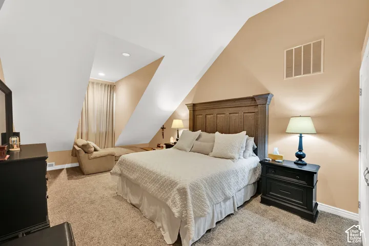 Vaulted ceiling with recessed lighting, angled walls, wood-finish headboard, built-in air vent, and neutral carpeting