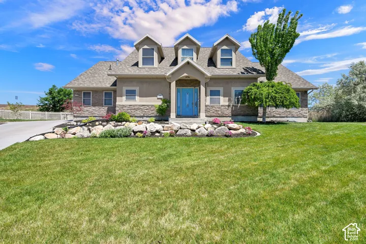 Stone veneer accents on the facade, stucco exterior finish, dormer windows, a prominent front door, and a landscaped rock garden
