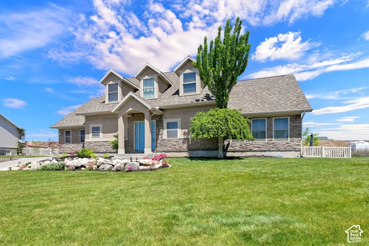 Stone and stucco exterior, dormer windows, covered entry, front landscaping with rock features, and a manicured lawn