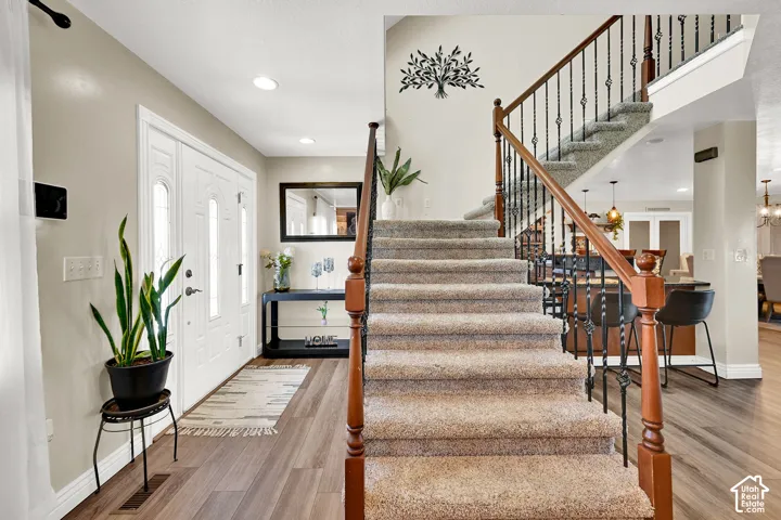 Entryway featuring a double door with decorative glass inserts, wood-finish flooring, recessed lighting, and a carpeted staircase with wrought iron balusters and a wood handrail
