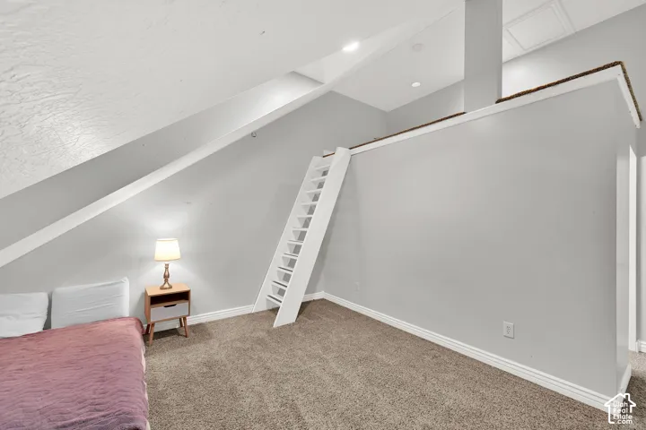Sloped ceiling room featuring carpet flooring, crisp white trim, and a built-in ladder accessing an elevated area