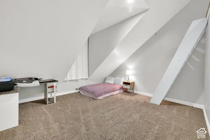 Carpeted attic space featuring sloped ceilings, a window with a white curtain, and light-colored wall paint