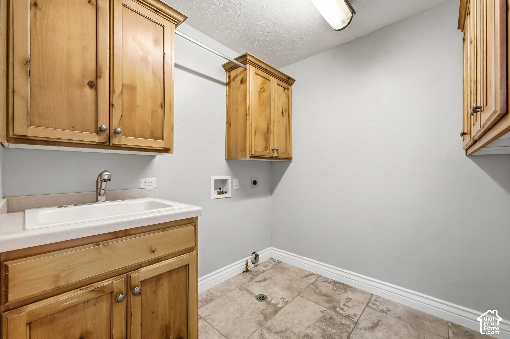 Light-toned tiled flooring, wood-finish cabinetry, built-in sink with faucet, white countertop, and overhead lighting fixture