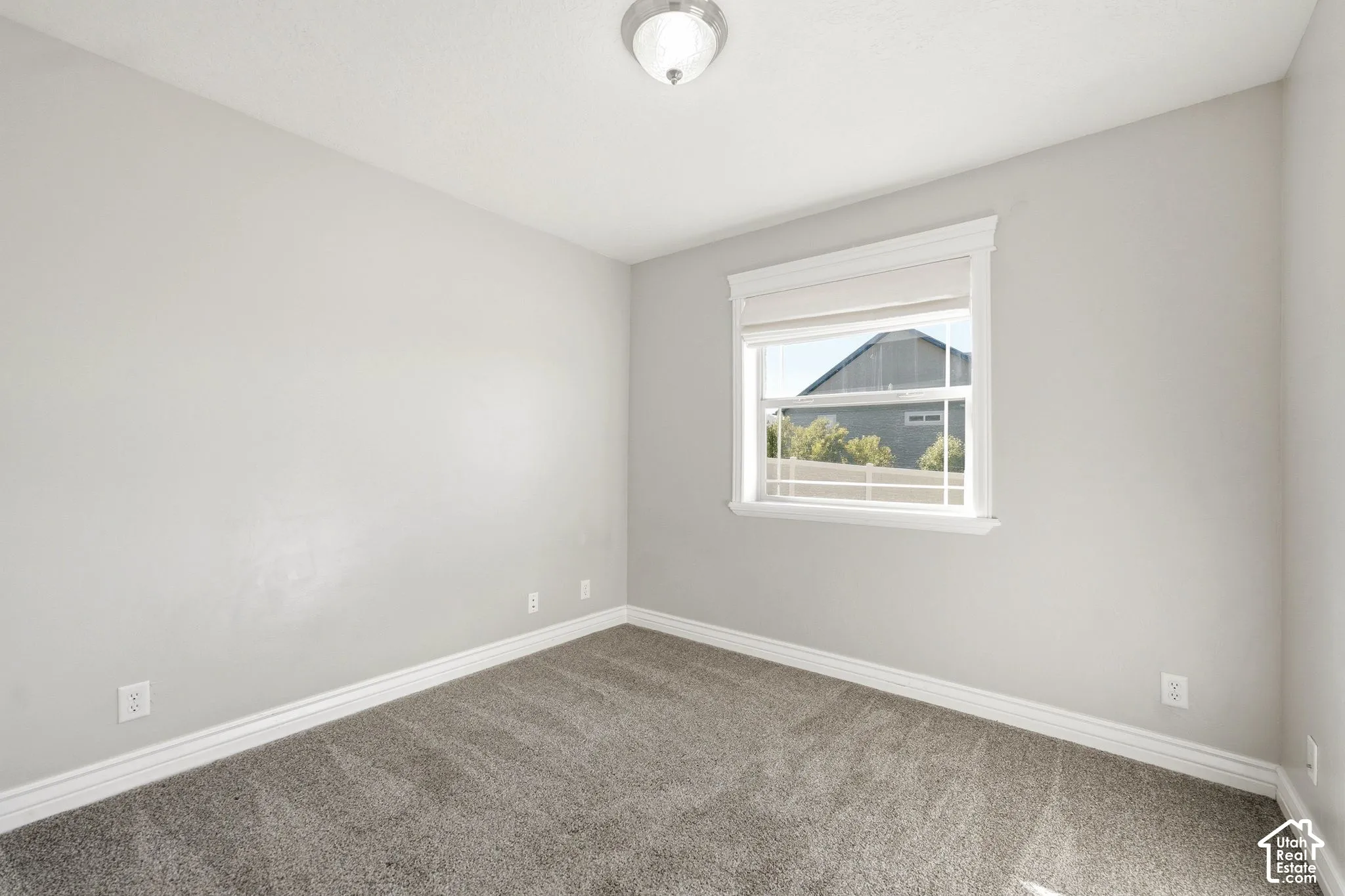 Neutral-toned walls, gray carpet flooring, and a single window with white trim