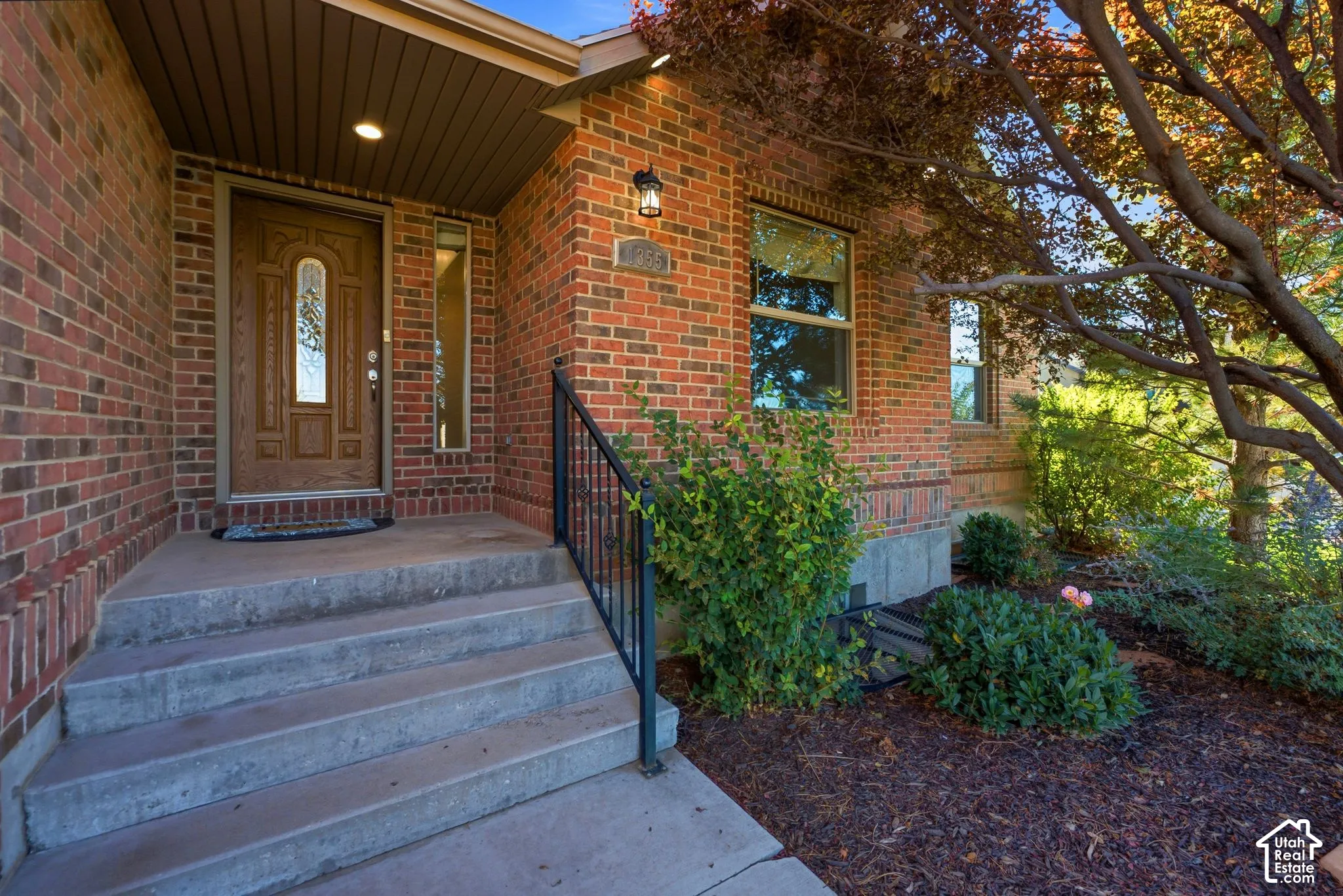 Brick exterior with a wooden entry door, sidelight, and concrete steps with a black metal handrail
