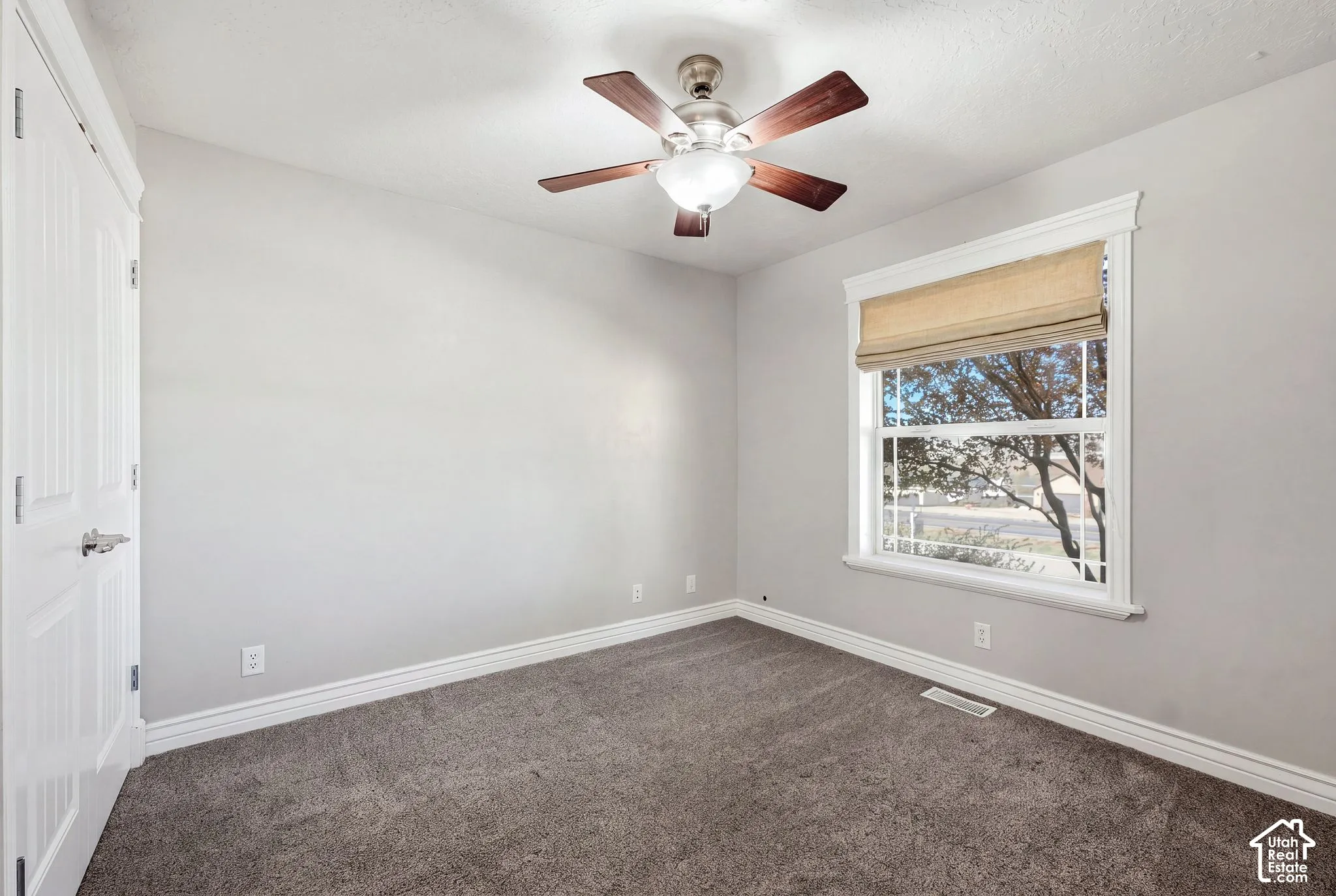 Window with privacy blind, ceiling fan with integrated lighting, textured gray carpeting, and white trim