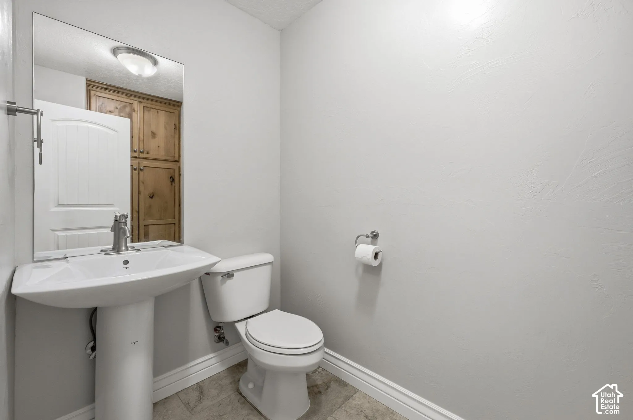 Pedestal sink with chrome faucet, toilet, and light-toned wall finish