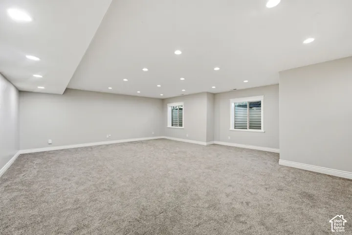 Expansive carpeted area with recessed lighting, light gray walls, and two windows with white trim