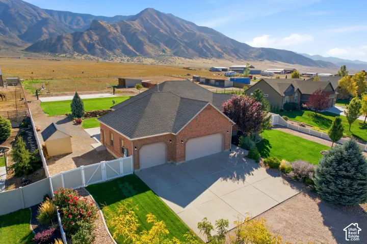 Brick exterior with an attached two-car garage, mature landscaping, paved driveway, and a white privacy fence