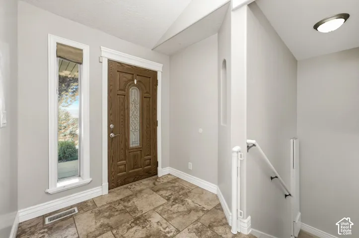 Front entry with a wood-paneled door featuring decorative glass, a sidelight window, and patterned tile flooring