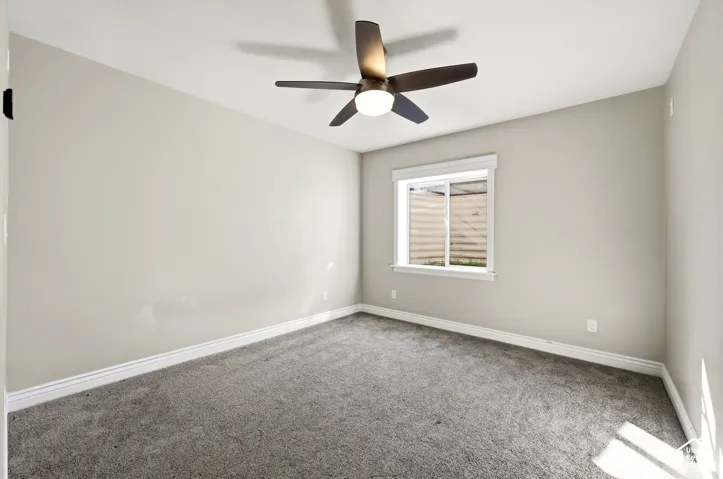 Plush carpet flooring, neutral wall paint, ceiling fan with integrated lighting, and a single window with blinds
