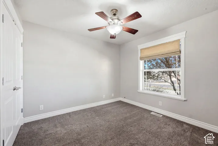 Window with privacy blind, ceiling fan with integrated lighting, textured gray carpeting, and white trim