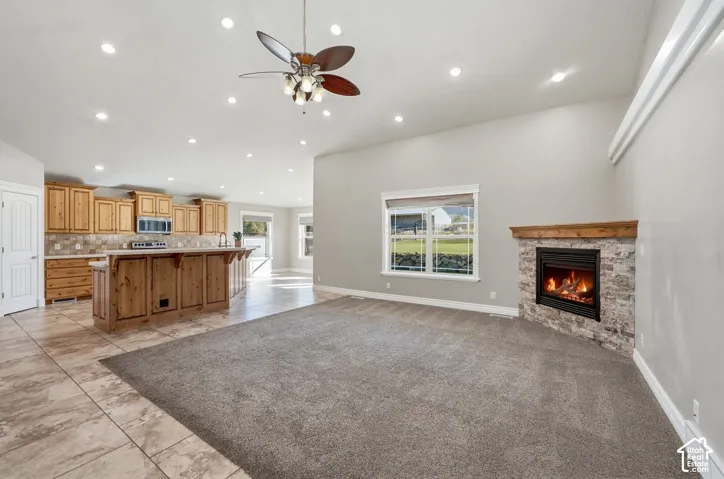 Open concept living space featuring a stone-clad fireplace with wood mantle, vaulted ceiling, and recessed lighting