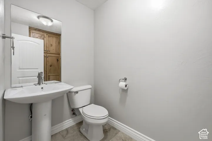 Pedestal sink with chrome faucet, toilet, and light-toned wall finish